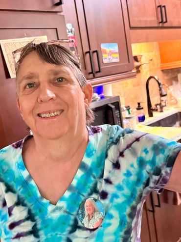 Smiling woman in tie-dye shirt taking a selfie in the kitchen.