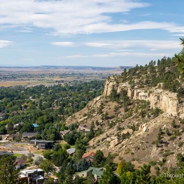 View of a town nestled near rocky cliffs and greenery under a partly cloudy sky.