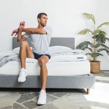 Man stretching arm while sitting on bed in a modern bedroom.