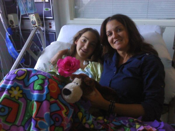 A girl and woman smiling in hospital bed with colorful blanket.