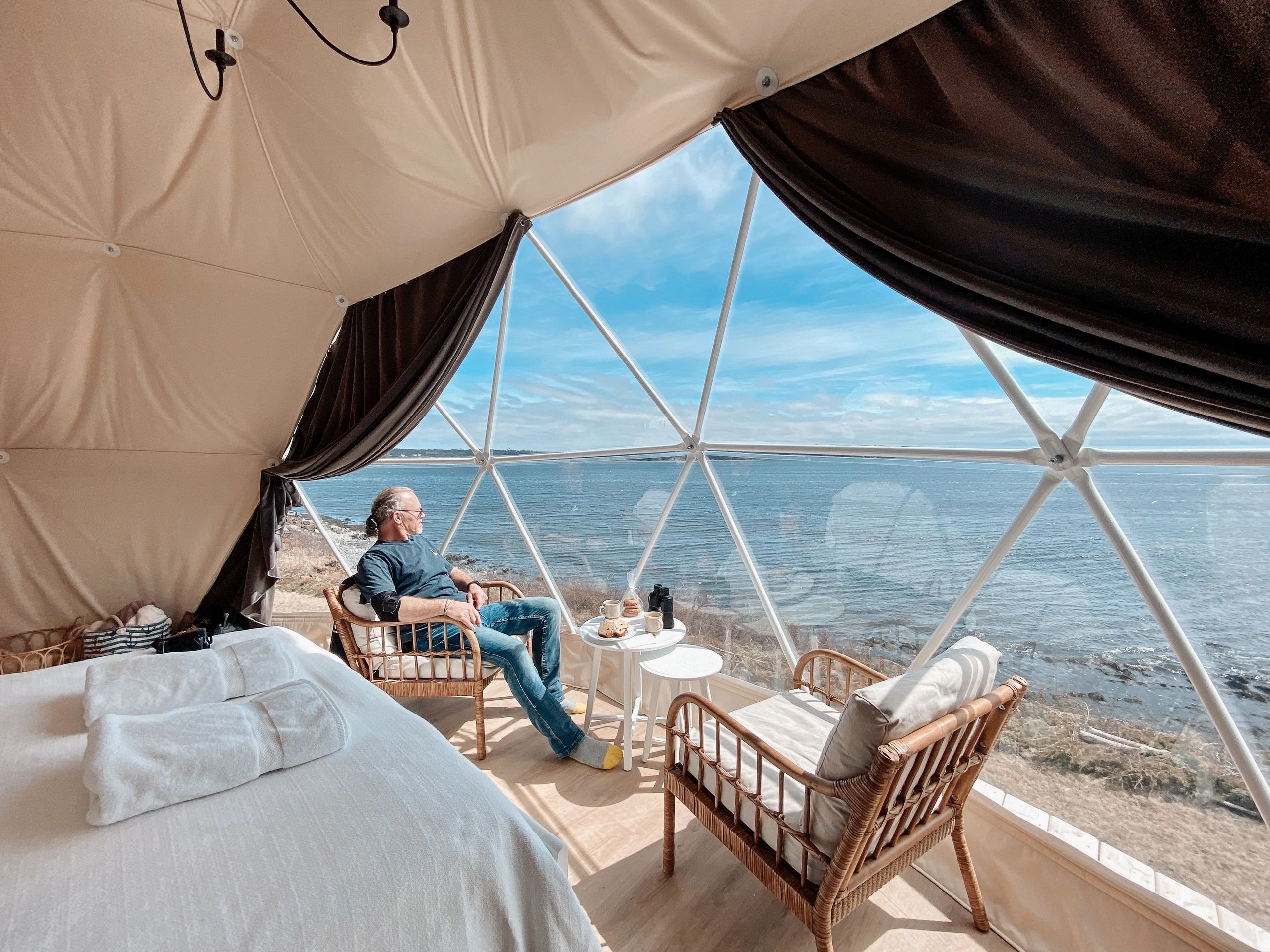 Man sits in Nova Scotia glamping dome taking in the expansive ocean views from inside the dome.
