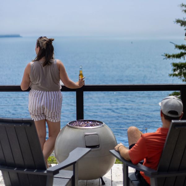 Woman holding a drink, viewing the ocean from a Nova Scotia glamping dome, while a man sits nearby.