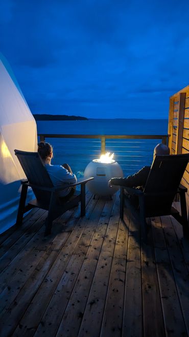 Nova scotia glamping dome private deck with couple in muskoka chairs and fire table overlooking ocea