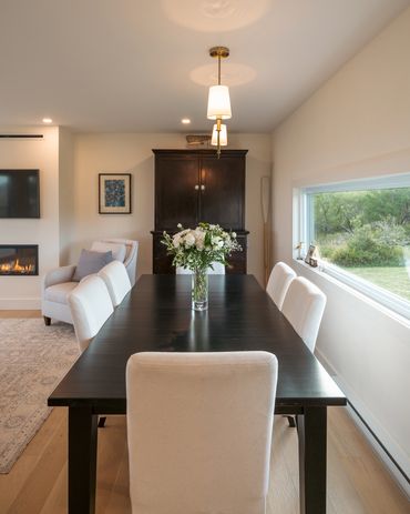 nova scotia cottage dining area with table, chairs and hutch. fireplace and picture window.