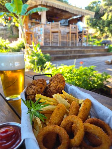Basket of fried appetizers with drinks in an outdoor setting.