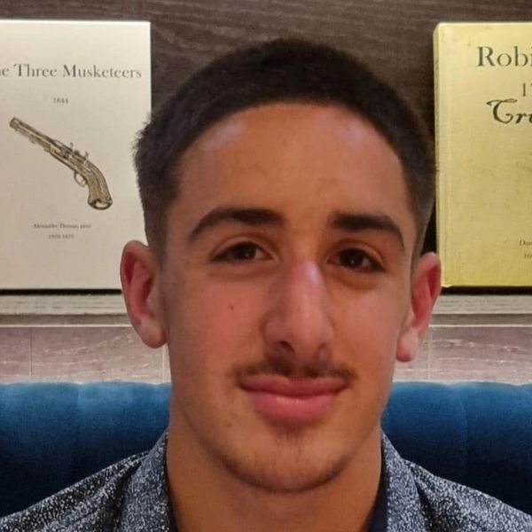 Young man with a subtle smile and trimmed mustache.
