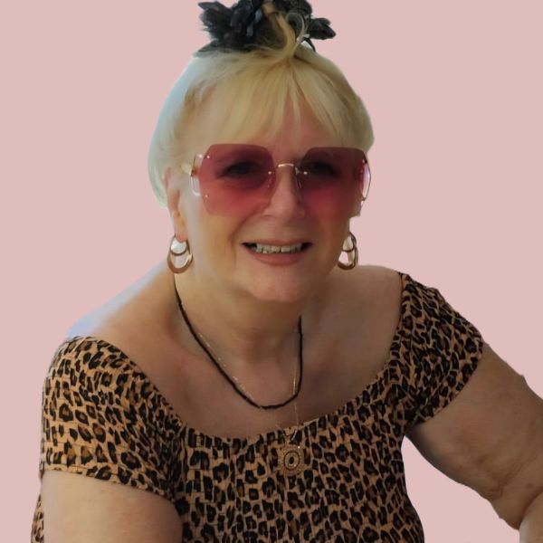 Smiling elderly woman wearing a leopard print dress and pink sunglasses.