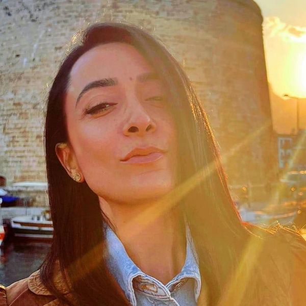 Woman taking a sunlit selfie near a stone building.