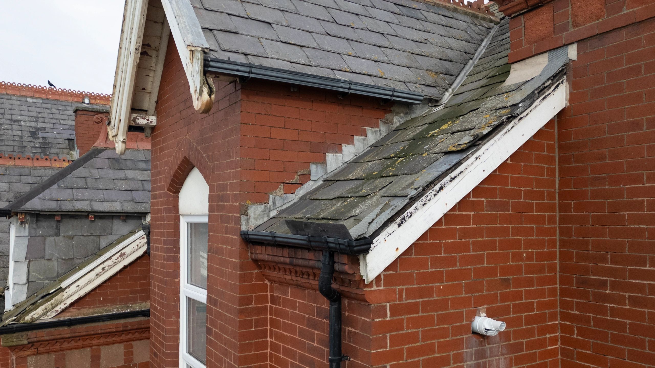 Old brick building with weathered slate roofs and black gutters.