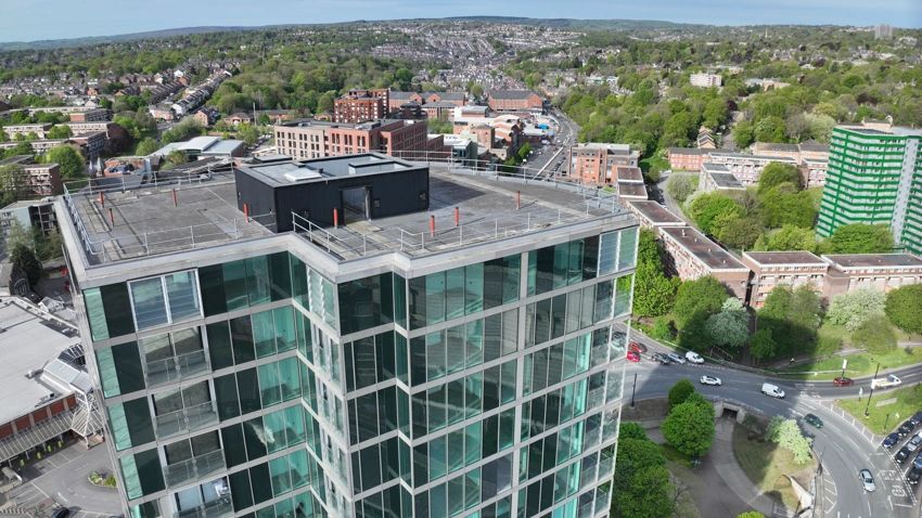 A tall glass building overlooking a green urban area with roads and houses.