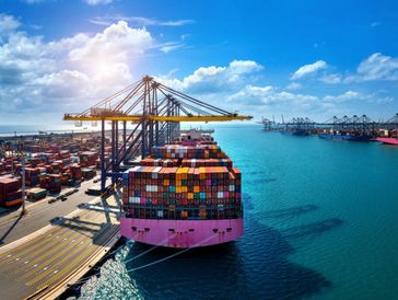 Cargo ship docked at container port under a sunny sky.