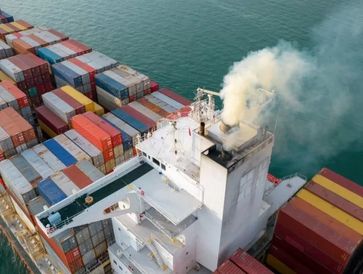 Smoke rising from a ship's funnel amid stacked cargo containers.