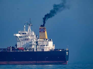 Large cargo ship emitting black smoke from its smokestack.
