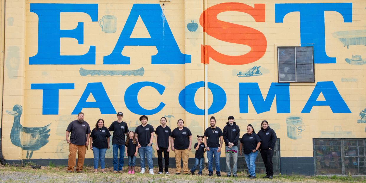 Group of people standing in front of a large mural that says EAST TACOMA.