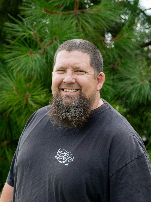 Smiling man with a beard wearing a black T-shirt outdoors.