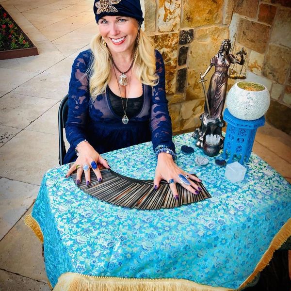 Smiling woman in blue with tarot cards spreads them on a floral tablecloth.