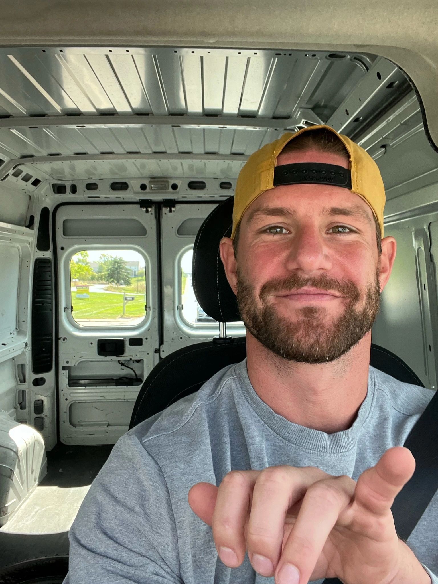 Smiling man in a yellow cap inside an empty van.