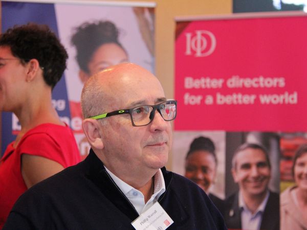 Philip is pictured wearing glasses looking to the side. Behind him the red IoD banner is visible.