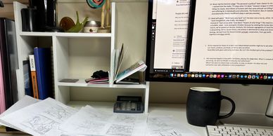 A cluttered desk with sketches, a calculator, a coffee mug, and a computer monitor displaying text.