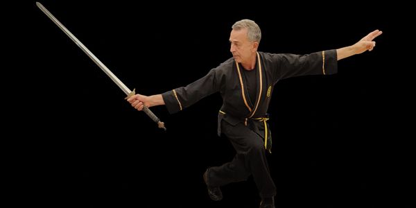 Man practicing martial arts with a sword against a black background.