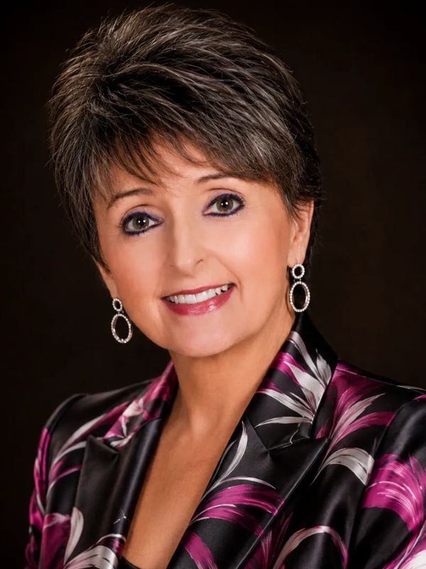 Professional woman with short hair, wearing a floral blazer and earrings, smiling warmly.