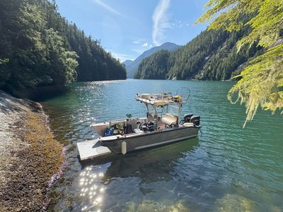 A boat floating on a calm lake surrounded by forested mountains.