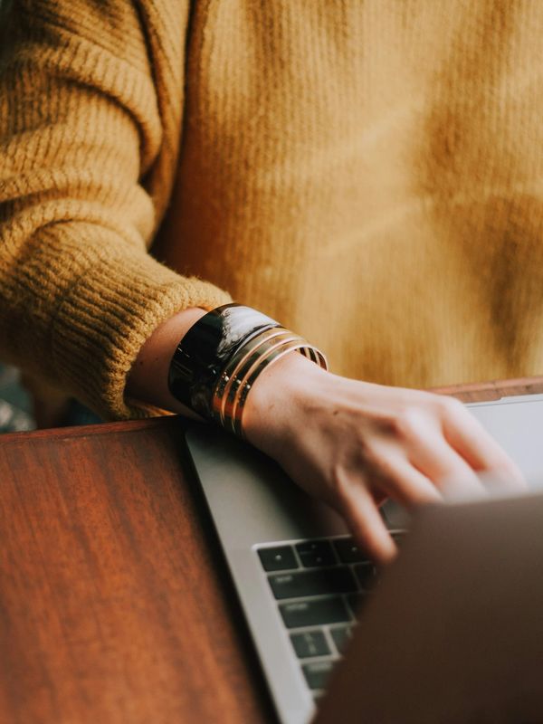 Person wearing a cozy mustard sweater using a laptop.