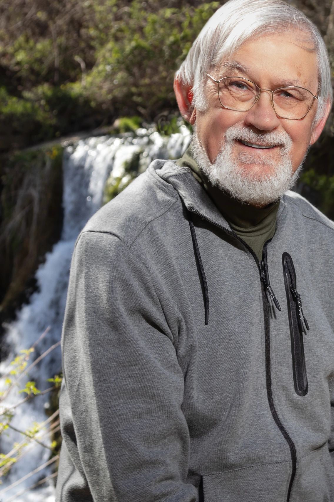 Smiling elderly man outdoors near a waterfall.
