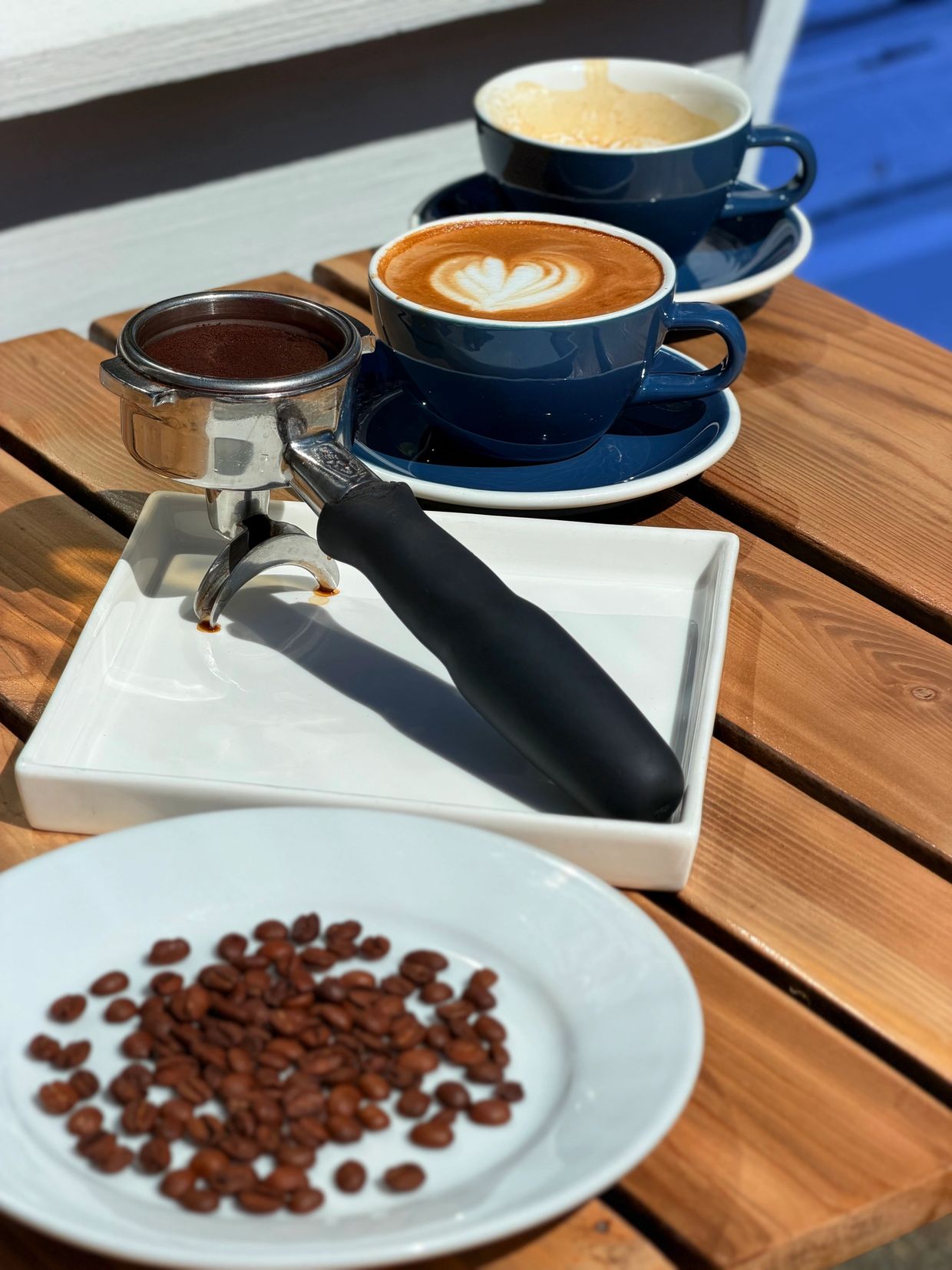 Two cups of coffee, coffee beans, and a portafilter on a wooden table.