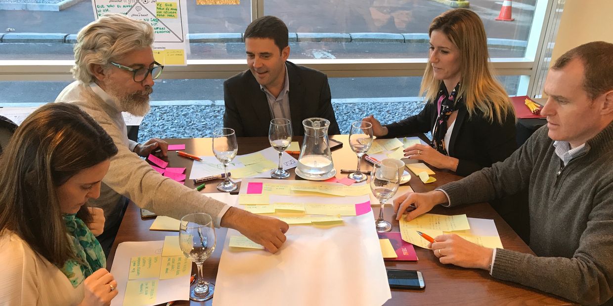 Três homens e duas mulheres sentados à mesa em uma reunião mexendo em papéis.