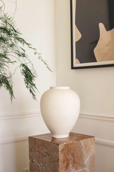 Minimalist white vase on a marble pedestal with abstract art and greenery.