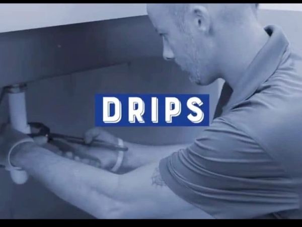 Technician fixing a plumbing drip under a sink.