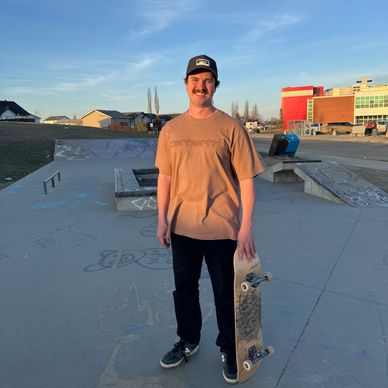 Young man holding skateboard at a skatepark during sunset.