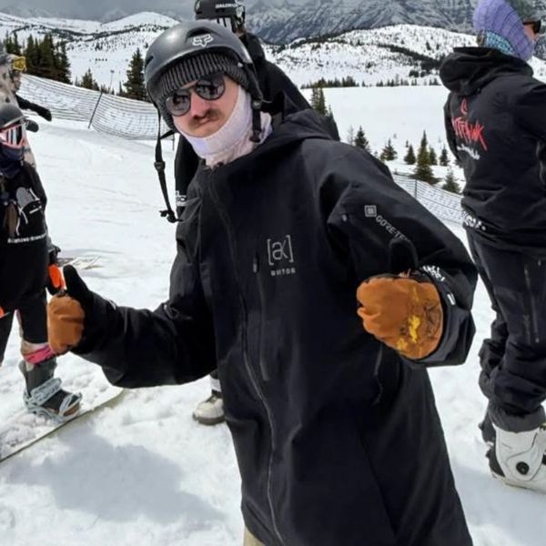 Person in black ski jacket and helmet giving thumbs up on snowy mountain.