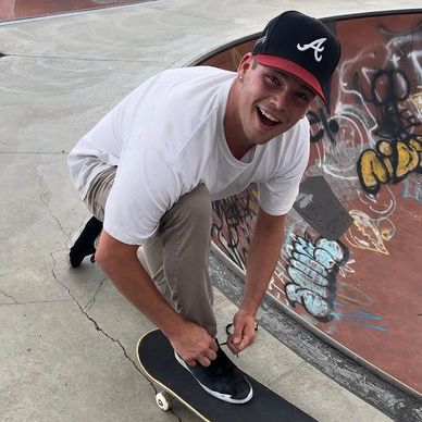 Young man tying shoelace on skateboard at skatepark with graffiti.