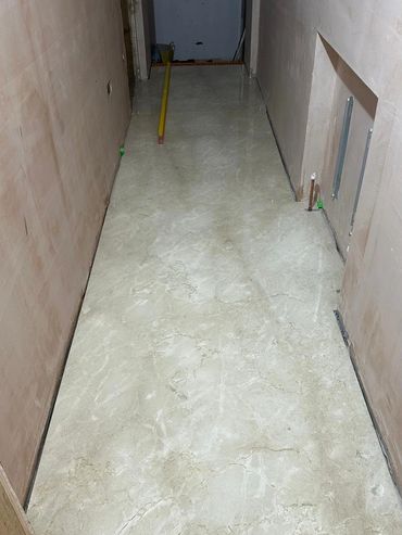 Newly installed marble floor tiles in a narrow hallway under renovation.