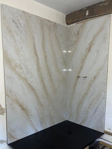 A partially installed shower with marble walls and a black base in a rustic room.
