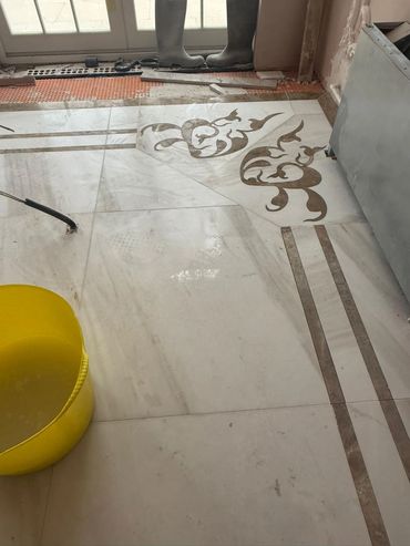 Partially installed decorative floor tiles with a yellow bucket and rubber boots nearby.