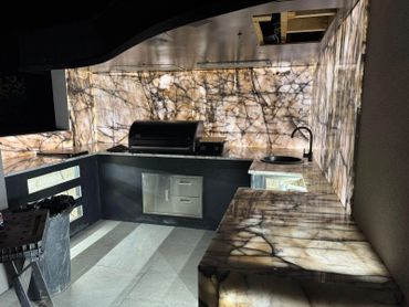 Modern outdoor kitchen with marble countertops and grill under warm lighting.