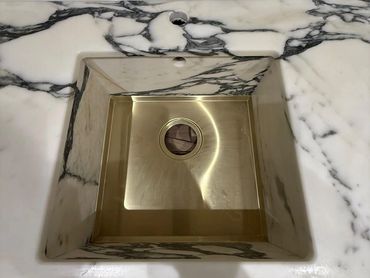 Square brass sink set in a white marble countertop with black veining.