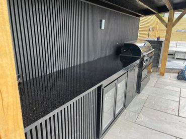 Modern outdoor kitchen with black granite countertop and built-in grill.