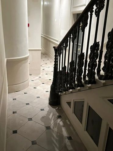 Elegant staircase with ornate black railing and polished marble floor.