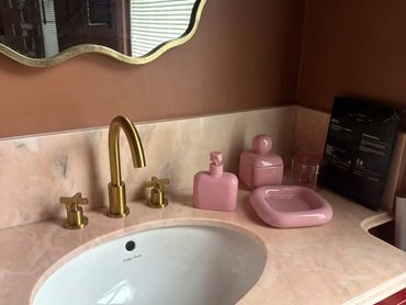 Bathroom sink area with gold faucet and pink accessories.