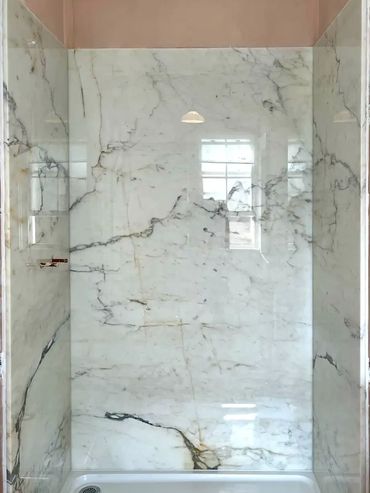 Elegant shower with white marble walls and a glass door.