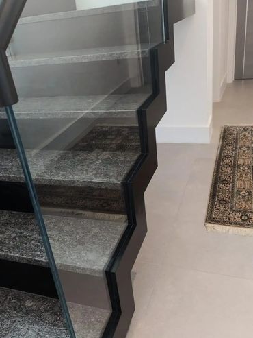 Modern staircase with glass railing and stone steps in a sleek interior.