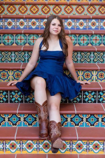 Young woman in blue dress and boots sitting on colorful tiled stairs.