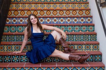 Young woman in a blue dress and boots posing on decorative tiled stairs.