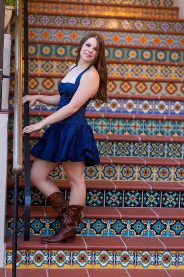 Woman in blue dress and boots on colorful tiled stairs.