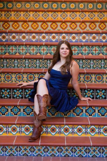 Woman in blue dress and boots on colorful tiled stairs.