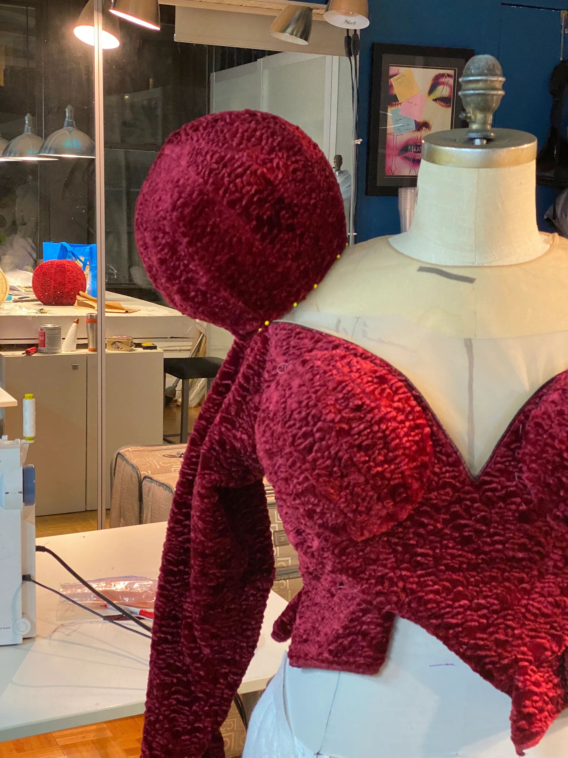Red textured garment on a dress form in a workspace.